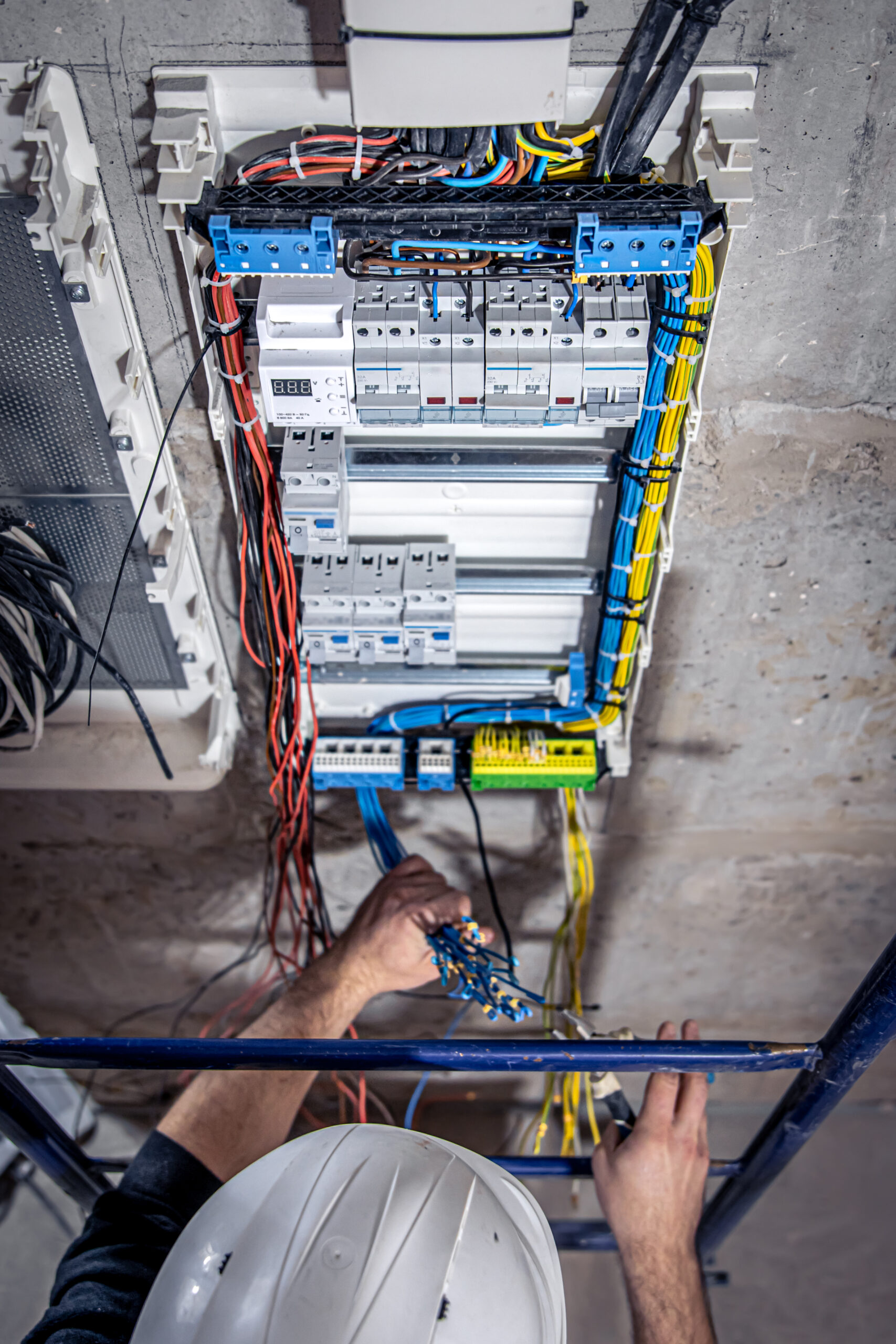 A male electrician works in a switchboard with an electrical connecting cable. A male electrician works in a switchboard with an electrical connecting cable, connects the equipment with tools, top view.