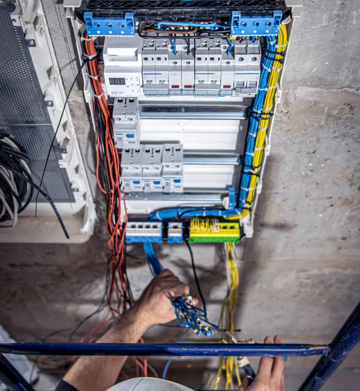 A male electrician works in a switchboard with an electrical connecting cable. A male electrician works in a switchboard with an electrical connecting cable, connects the equipment with tools, top view.